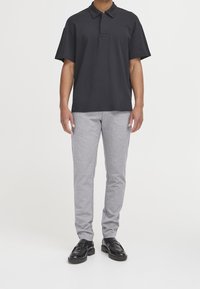 Polo shirt noir à manches courtes avec un col replié, associé à un pantalon de jogging slim gris clair et des chaussures en cuir noires.