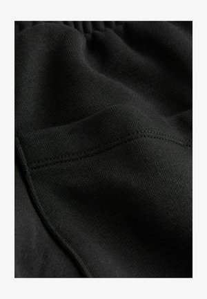 Melns audums, cieši austs ar gludu tekstūru. Redzams elastīgs jostasvērts ar kontrastējošo šuvju apdari gar malām.