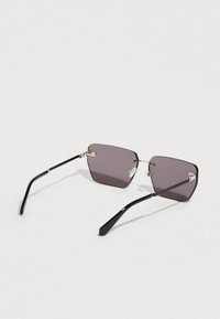 Ochelari de soare negri cu o formă geometrică, lentile gri închis, brațe negre subțiri și accente aurii la balamalele ramei.