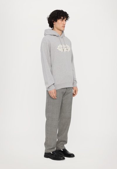 Grauer Hoodie mit Frontstickerei, kombiniert mit karierter grauer Hose. Schwarze Schuhe runden das Outfit ab. Minimalistisches Design und lockere Passform.