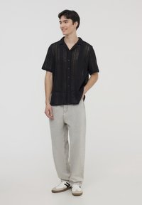 Maglietta nera a manica corta con fori e colletto; abbinata a jeans grigi chiari a vestibilità ampia e sneakers bianche con dettagli neri.