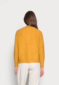 Senapsgul stickad tröja med avslappnad passform, rund halsringning och ribbade manschetter. Mjuk textur och kort längd.