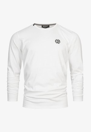 Vit långärmad t-shirt i bomull, med rund halsringning och en liten svart logga på vänster bröst. Slät struktur.