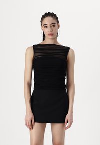 Rochie neagră cu o siluetă ajustată, textură pliată la bust și detalii transparente suprapuse pe umeri. Pantaloni scurți.