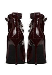 Chaussures à talons hauts en cuir verni bordeaux avec des brides de cheville et des talons pointus, présentant une finition brillante et des accents de semelle noire.