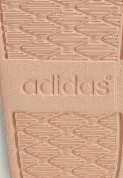 Semelle de sandale Adidas en rose clair, présentant un motif texturé avec des formes en losange et des lignes horizontales, nom de la marque embossé sur le côté.