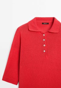 Czerwony dzianinowy top polo z kołnierzykiem, krótkimi rękawami i czterema białymi guzikami na plisie. Miękka faktura i luźny krój. Widoczna metka marki.