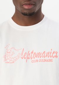 White cotton t-shirt featuring pink graphic print of a cartoon shrimp and the text “leptomanicx CLUB CULINAIRE” below. Round neckline.