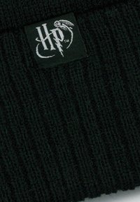 Schwarze Strickmütze mit vertikaler Rippstruktur und einem rechteckigen Etikett mit weißer Schrift und grafischem Design.