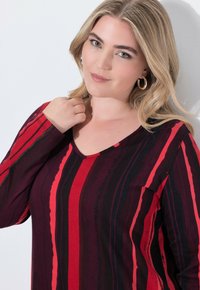 Long-sleeve top in red, black, and burgundy stripes, featuring a V-neckline and a smooth, soft texture.