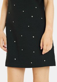Vestido negro texturizado con brillantes plateados dispersos, de longitud por encima de la rodilla, con una silueta sencilla y ajustada y mangas cortas.
