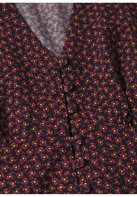 Gros plan d'un tissu noir avec un petit motif floral rouge, violet et beige et des boutons recouverts de tissu le long d'un col en V.