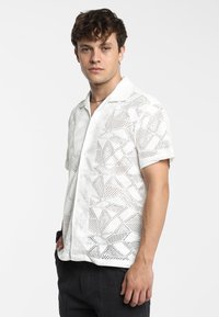 Witte korte mouwen shirt met een gestructureerd geometrisch patroon, knoopsluiting en een kraag. Gekozen met donkere broek, wat een relaxte pasvorm laat zien.