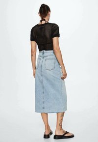 Mustat neulotut crop topit, joissa on lyhyet hihat, yhdistettynä korkeavyötäröiseen, vaaleansinisestä denimistä valmistettuun kynähameeseen, jossa on raakareuna ja takataskut.