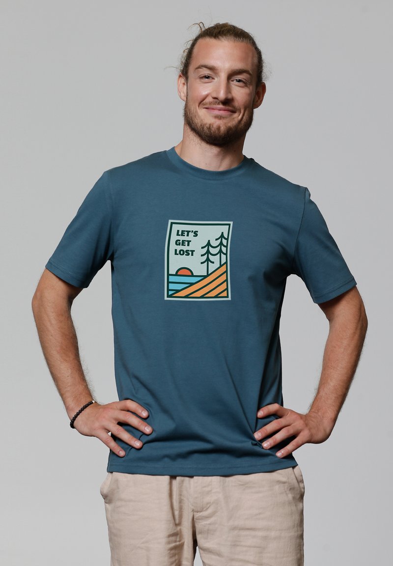Blaue Baumwoll-T-Shirt mit einem grafischen Design, das den Text "LASST UNS VERLIEREN" zeigt, sowie Bäume, eine Sonne und gestreiftes Land in erdigen Tönen.