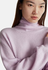 Jasnofioletowy sweter z golfem wykonany z miękkiej, teksturowanej tkaniny. Posiada prążkowany dekolt i luźno dopasowane rękawy.