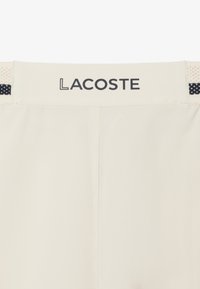 Pantalones cortos blancos de Lacoste con una cintura plana con el logo, detalle texturizado y acentos negros cerca de la parte superior. Acabado de tela suave.