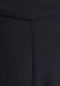 Tecido preto em primeiro plano com uma superfície texturada apresentando linhas verticais. O material parece suave, com um ligeiro brilho e é leve.