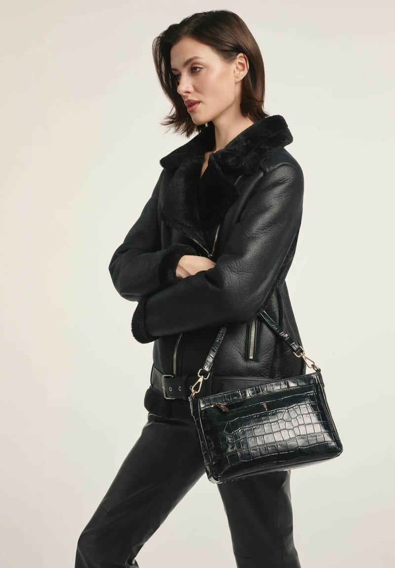 Czarna skórzana kurtka z owczej wełny z zamykanymi kieszeniami; modelka trzyma czarną, teksturowaną torebkę z sztucznej skóry krokodyla z srebrnymi akcesoriami.
