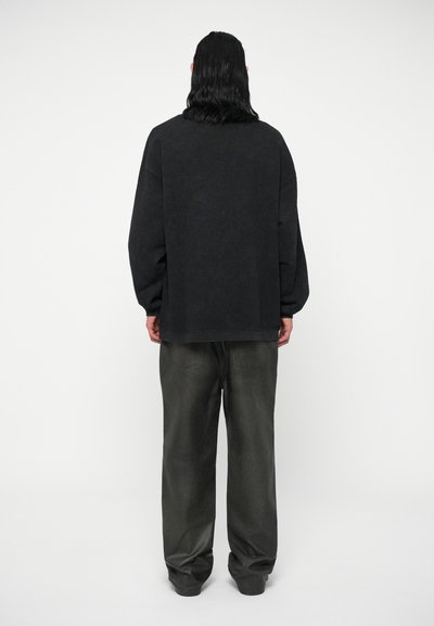 Pullover nero oversize con spalle cadenti, abbinato a pantaloni larghi color carbone. Il materiale sembra morbido e testurizzato.