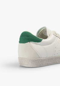 Baskets blanches avec semelle texturée, talon en daim beige et languette de talon en daim vert avec détail de logo cousu.
