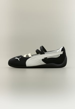 Black and white Puma slip-on shoe with two black elastic straps and one white strap over the top, textured sole, and Puma logo near toe.