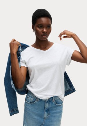 White cotton V-neck t-shirt paired with a light blue denim skirt, holding a dark denim jacket. Smooth texture, casual fit, classic design.
