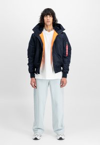 Marine bomberjakke med oransje fôr, glidelåslukking og sidelommer; kombinert med en hvit T-skjorte og lyseblå vide jeans.