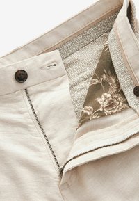 Pantaloni bej cu fermoar și închidere cu nasture, având un model floral intricată pe banda interioară a taliei. Textură fină din in.