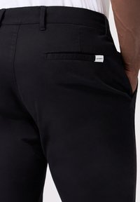 Pantaloni neri realizzati in un tessuto liscio, con una tasca posteriore e una piccola etichetta bianca del marchio. Design semplice e sartoriale.