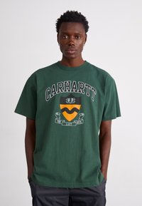  Zielona bawełniana koszulka z krótkim rękawem, z dużym nadrukiem graficznym z napisem "Carhartt" oraz wzorem tarczy w pomarańczowym i czarnym kolorze, okrągły dekolt.