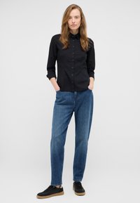 Black button-up shirt with long sleeves, paired with loose-fit blue denim jeans and black sneakers with a light brown sole.