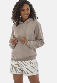 Lichtbruin hoodie met trekkoorden en geribde mouwen, gecombineerd met witte shorts met een bruin zebrapatroon en een witte bontafwerking.