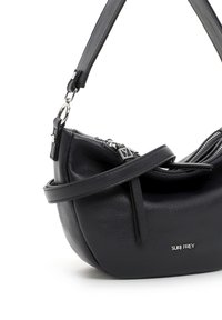 Väike must nahast õlakott hõbedase luku ja logoga, reguleeritava rihma ja ümarate põhjaosadega valgel taustal.