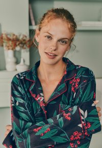 Námořnický pyžamový set s květinovým vzorem, který obsahuje zelené listy a červené bobule, doplněný červenými lemovkami na límci a manžetách.