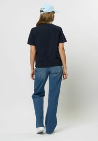 Mornarica majica uparena s širokim plavim trapericama, s opuštenim krojem. Na glavi je svijetloplava kapa s logotipom straga.