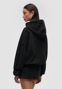 Czarna, oversize'owa bluza z kapturem i kieszenią z przodu, zestawiona z czarną spódnicą dżinsową z haftowanym logo.