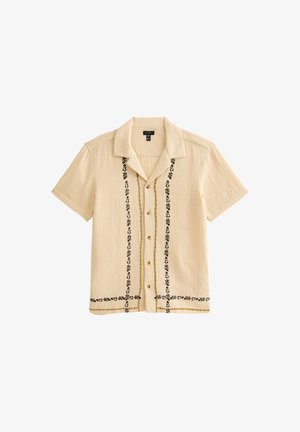 Short-sleeve beige shirt featuring textured fabric, black floral embroidery down the front, and brown buttons. Casual design with a collar.