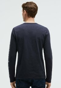 Marineblaues Langarm-T-Shirt aus weicher Baumwolle mit rundem Ausschnitt und einem bedruckten Design entlang des linken Ärmels. Glatte Textur.