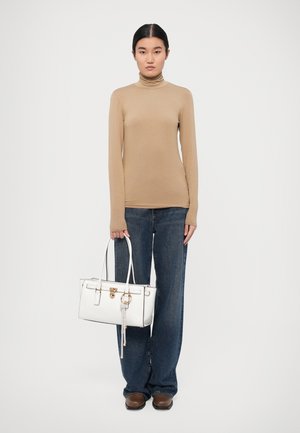 Tan long-sleeve turtleneck, dark blue wide-leg jeans, and a white leather handbag with gold hardware and a decorative keychain detail.