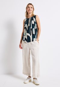 Top senza maniche con fantasia in navy, crema e teal. Abbinato a pantaloni larghi in lino color beige chiaro e sneakers bianche con suola spessa.