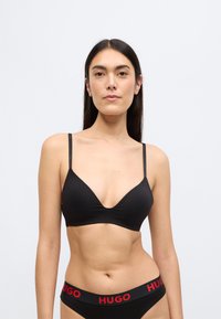 Czarny stanik z głębokim dekoltem i cienkimi ramiączkami, wykonany z gładkiego materiału; w komplecie czarne majtki z czerwonym napisem "HUGO".