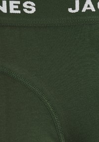 Dunkelgrüne Baumwollunterwäsche mit glatter Textur, ausgestattet mit einem weißen, gebrandeten Bund und verstärkten Nähten entlang der Kanten.