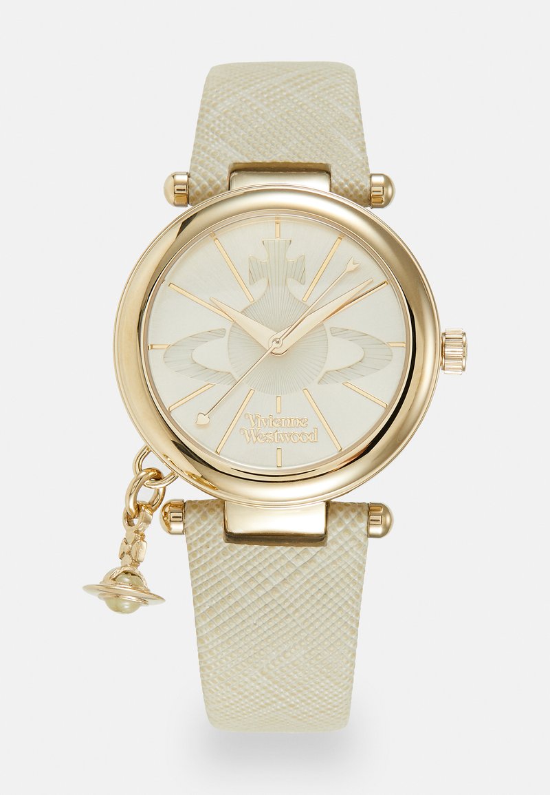 Auksinės spalvos laikrodis su tekstūruotu smėlio spalvos dirželiu, apvaliu ciferblatu ir sudėtingu šviesiai kreminiu ciferblatu, kuriame yra saulės spindulių raštas ir Vivienne Westwood logotipas.