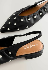 Svarta slingback-lägenheter med spetsig tå, prydda med silvernitar. Tillverkade av mjukt konstläder och ergonomisk sula för komfort.