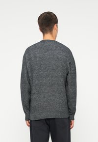 Πλεκτό πουλόβερ σε σκούρο γκρι, με υφασμάτινη υφή, στρογγυλή λαιμόκοψη και ριμπ μανσέ�τες στο κάτω μέρος και στα μανίκια.