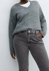 Suéter de punto acanalado gris con escote en V, combinado con jeans de mezclilla gris. La textura es suave y el corte es relajado.