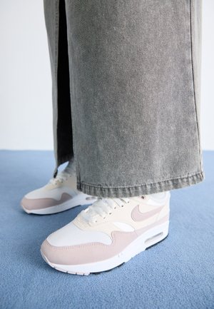 Witte en lichtroze Nike Air Max sneakers met een gestructureerde bovenkant en zichtbare luchtbel-details, gecombineerd met grijze denim broek.