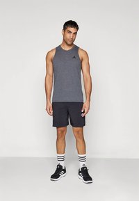 Sivý športový tielko, čierne šortky a čierne tenisky s bielymi pruhmi. Na tielku a šortkách je logo Adidas.