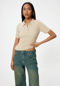 Beige geribbelde gebreide polo met korte mouwen, voorzien van een kraag en drie knopen. Gecombineerd met hoogwaist, lichtblauwe denim jeans.